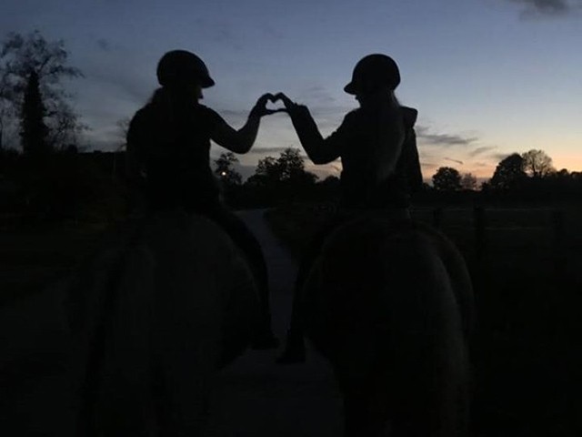 Zwei Reiterinnen formen bei Abendrot mit den Händen ein Herz